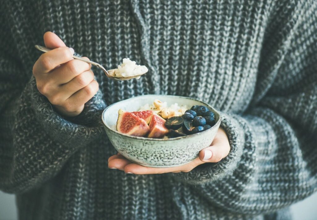 Hands holding a bowl of oatmeal with blueberries and fruit